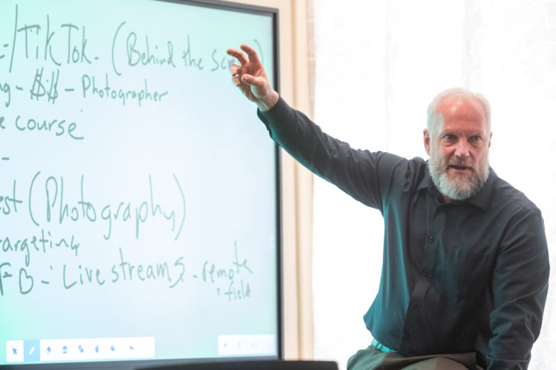Middle-aged white man with beard pointing at a smart board that contains handwritten social media strategies