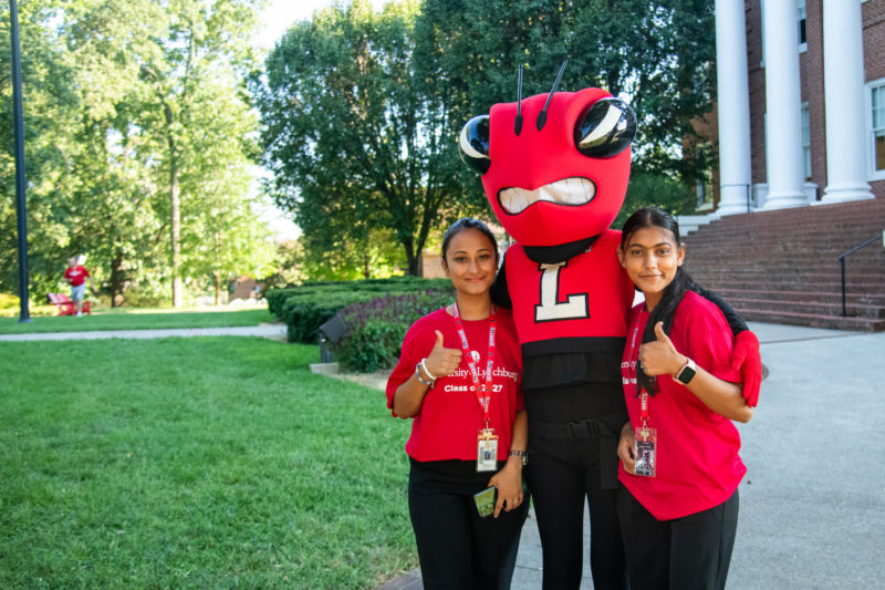 Two dark-skinned female students in red shirts outside with a Hornet mascot in red and black 