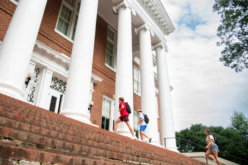 Three students walk up brick steps toward a large brick building with white columns