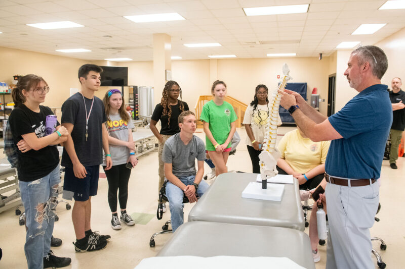 A group of high school students watch as a man shows them a skeleton in a lab