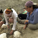 Professor Brooke Haiar points to a fossil on the ground beside a student