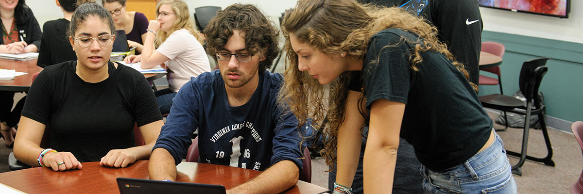 Students gathered around a table looking at a computer.