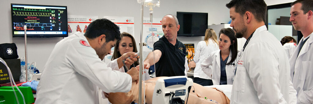 A group of students and a faculty member in a medical classroom are performing a medical procedure