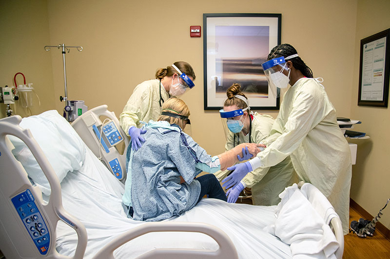 Three nursing students helping a patient out of bed