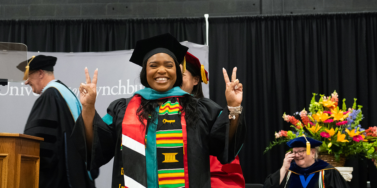 A female student holds up two fingers on each hand as she poses for a photo during commencement