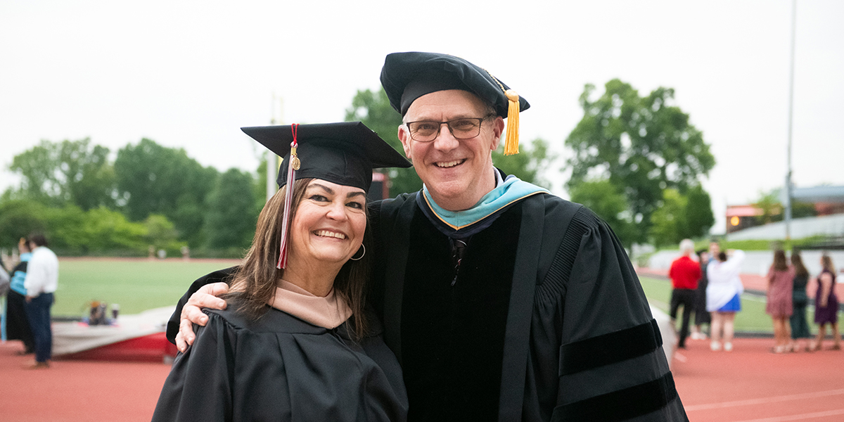 Two professors smile at the camera during commencement