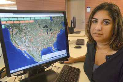 A brown-skinned woman with shoulder-long black hair sits at a computer showing a map