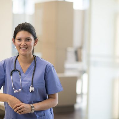 A doctor (dentist, or nurse) posing for a picture in a professional medical office setting with a stethoscope .