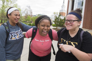 Three students with their arms over each other's shoulder. They are wearing sorority t-shirts and laughing.