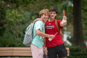 Two guys with their arms over each other's shoulder. They are holding popsicles one has it lifted toward the camera.