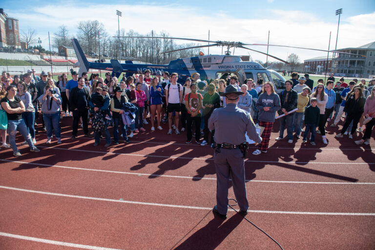 A Virginia state trooper talks to a crowd in front of a police helicopter
