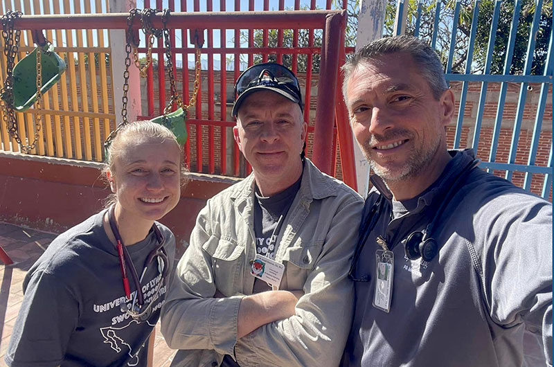 Three instructors pose in front of a playground.