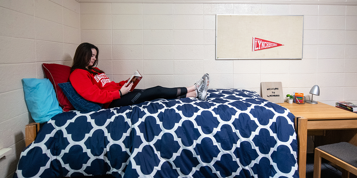 A student reads a book on her bed in Tate Hall
