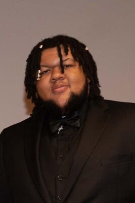 A young Black male with braids wearing a black suit