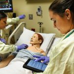 Nursing students using an iPad in a simulation center. One of the students is "treating" a mannequin.