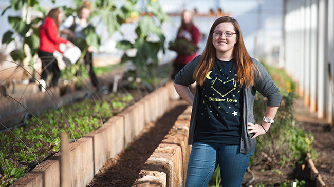 A student stands in a greenshouse.