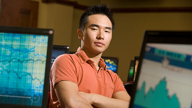 A Master of Business Administration (MBA) student stands in front of computer screens.