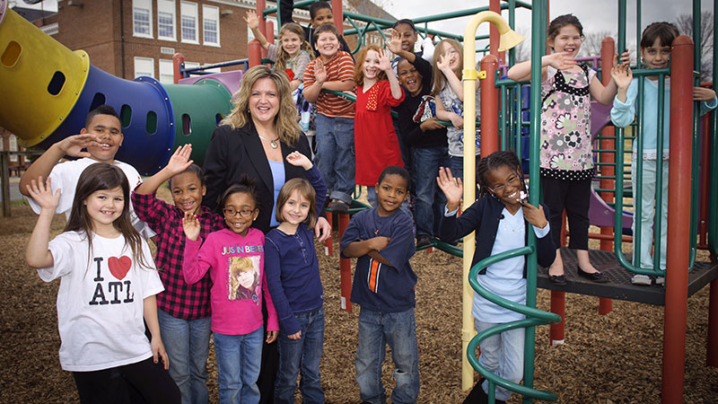 A woman standing in a playground, surrounded by children