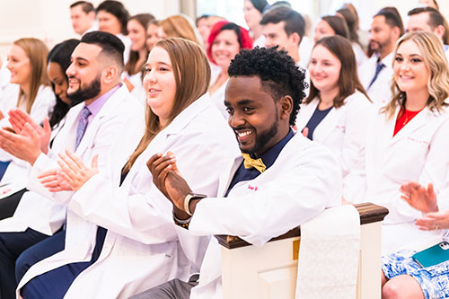 Students clap in audience wearing white coats