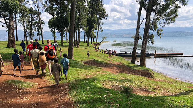 An MPH student walks with children along a river in Rwanda