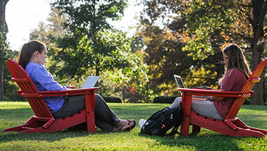 Two students sit on red chairs.