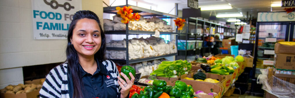 A student holding a bell pepper while standing in a food pantry