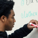 A student is writing in Spanish on a whiteboard