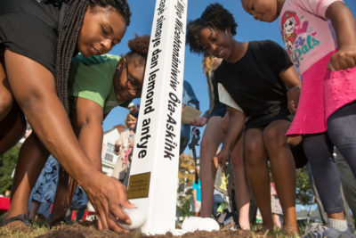 Students gather around a peace pole putting rocks at the base.
