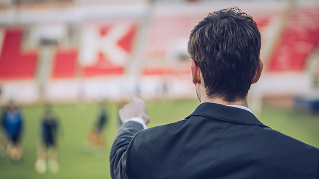 A man from behind as he points at a sports field in the distance