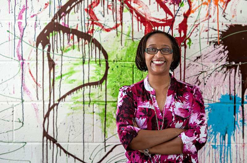 A woman stands in front of a wall splattered with paint