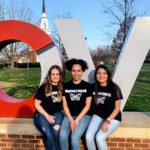 Three students sit at the LOVE statue