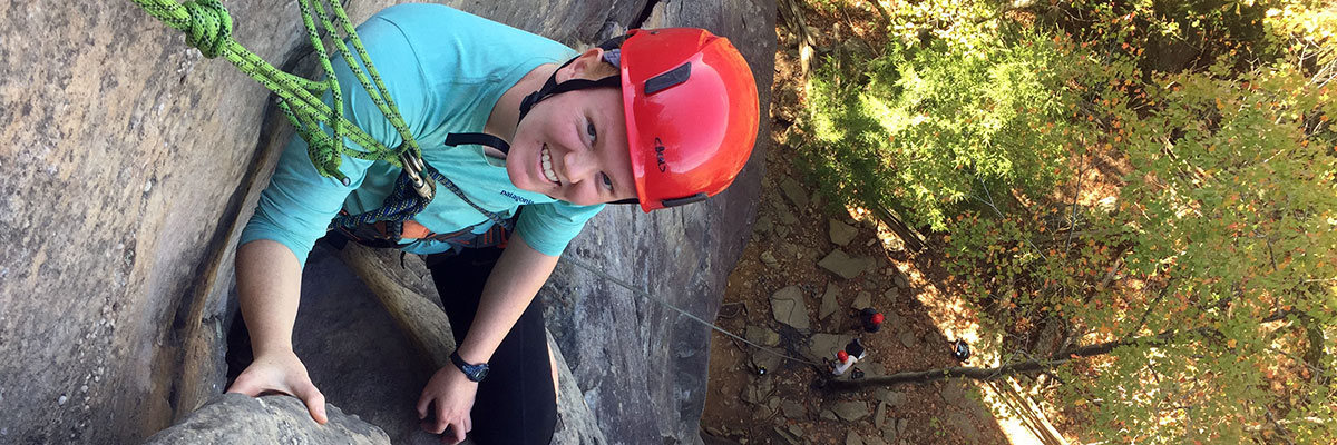 Natalie Hanno '21 climbing a rock and looking up at the camera